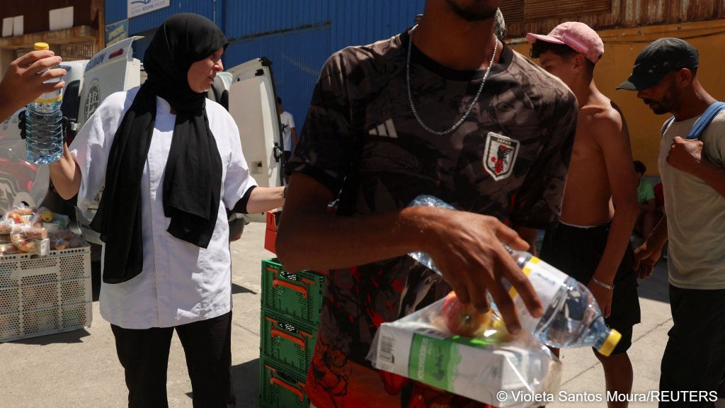 Migrants receive food staples from local NGO Media Luna Blanca in an industrial area where they are sleeping amid recent mass crossings by migrants on foot and by sea from Morocco into the Spanish territory, in Ceuta, Spain, August 6, 2026 | Photo: REUTERS/Violeta Santos Moura