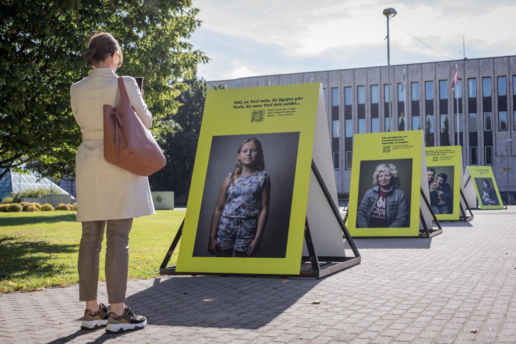 A woman standing in front of a portrait of an Ukrainian refugees at the the Brothers and Sisters photo exhibition in Riga | Photo: Martin Thaulow
