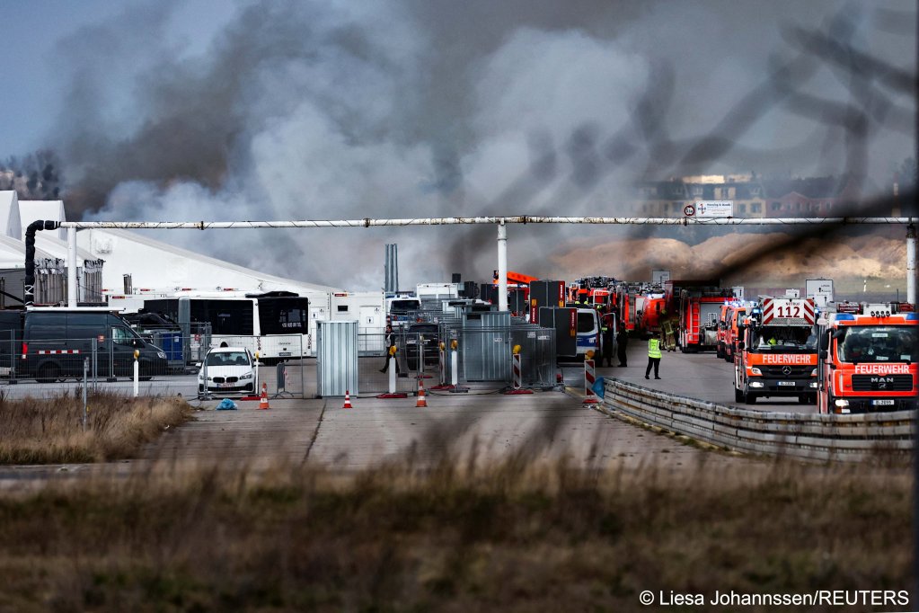 Firefighter vehicles are lined up as smoke billows from a tent for migrants at the former Tegel airport in Berlin, Germany, March 12, 2024 | Photo: REUTERS/Liesa Johannssen