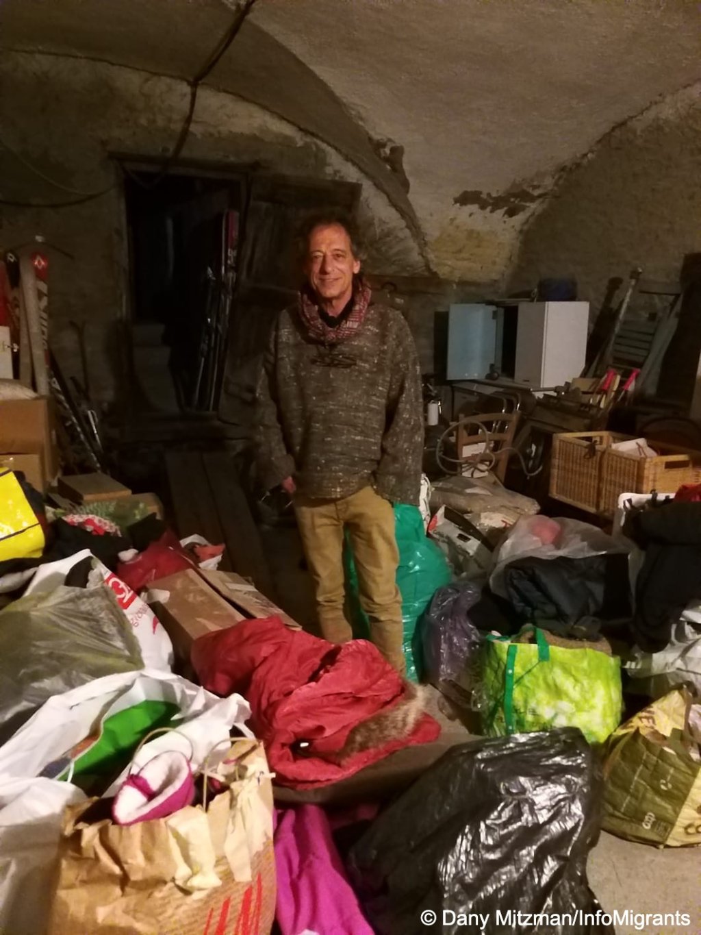 Anthropologist Piero Gorza stands in his garage surrounded by bags of donated clothing for migrants. He sometimes hosts families at his home when there is no room for them at the refuge | Photo: Dany Mitzman / InfoMigrants