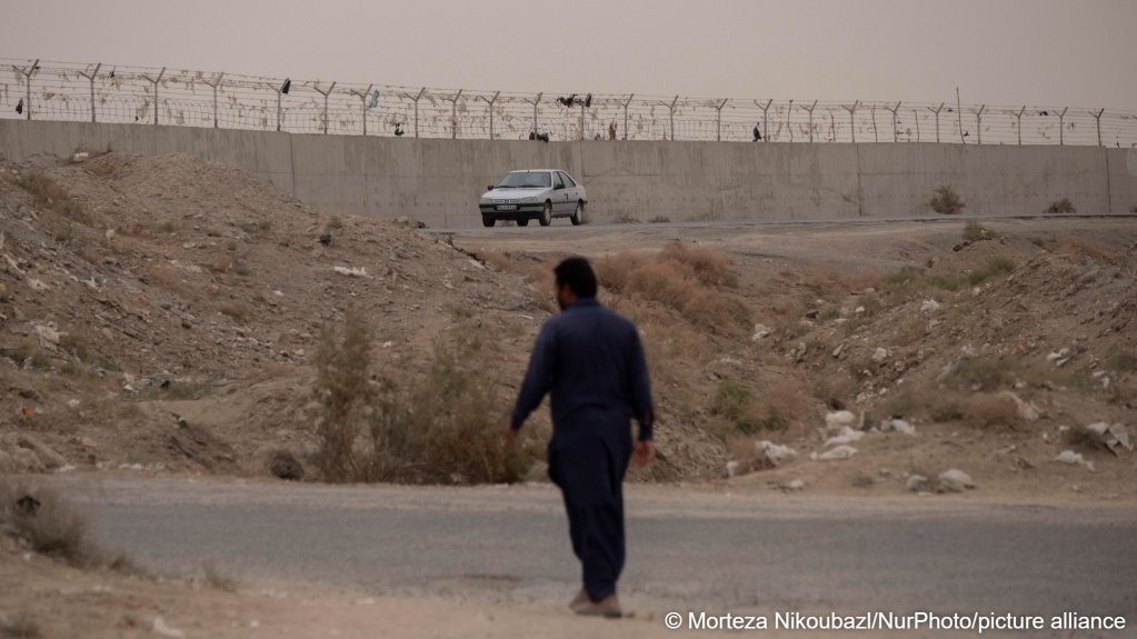 An Iranian Baloch man walks near a border wall on Iran's eastern border with Afghanistan, in Hirmand County, Sistan and Baluchistan Province, directly opposite Zaranj in Afghanistan's Nimruz Province | Photo: Morteza Nikoubazl / NurPhoto