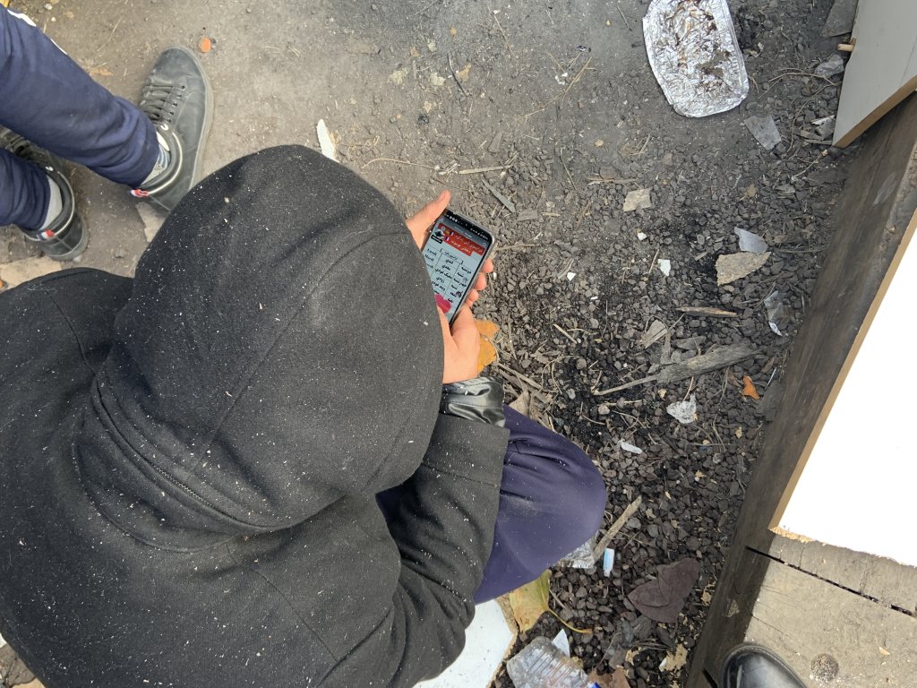 Un migrant à la rue à Paris consulte son téléphone. Crédit : InfoMigrants