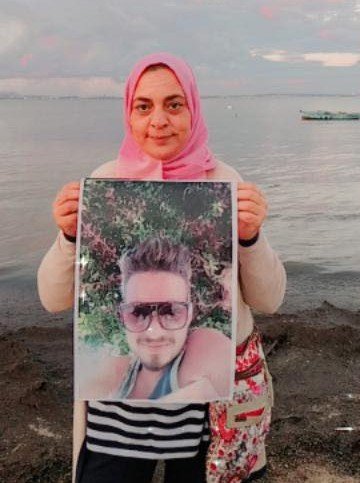 Jalila tient le portrait de ses fils, sur une plage tunisienne. Crédit : DR