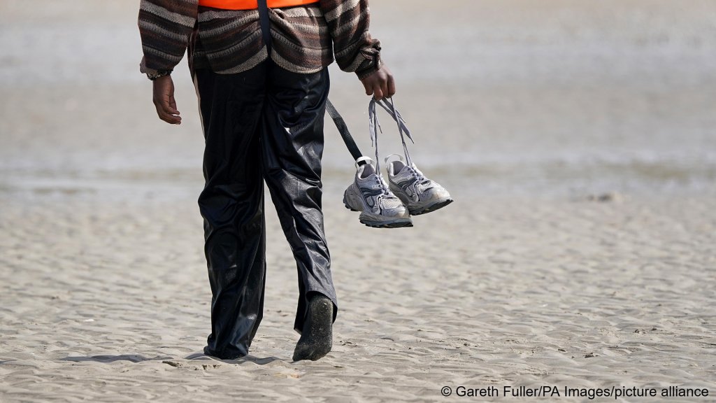 A person wearing a life vest and carrying their shoes, photographed as they leave the shore of Equihen-Plage, France, on July 22, 2026, after not making it onto a boat to cross the Channel | Photo: picture alliance