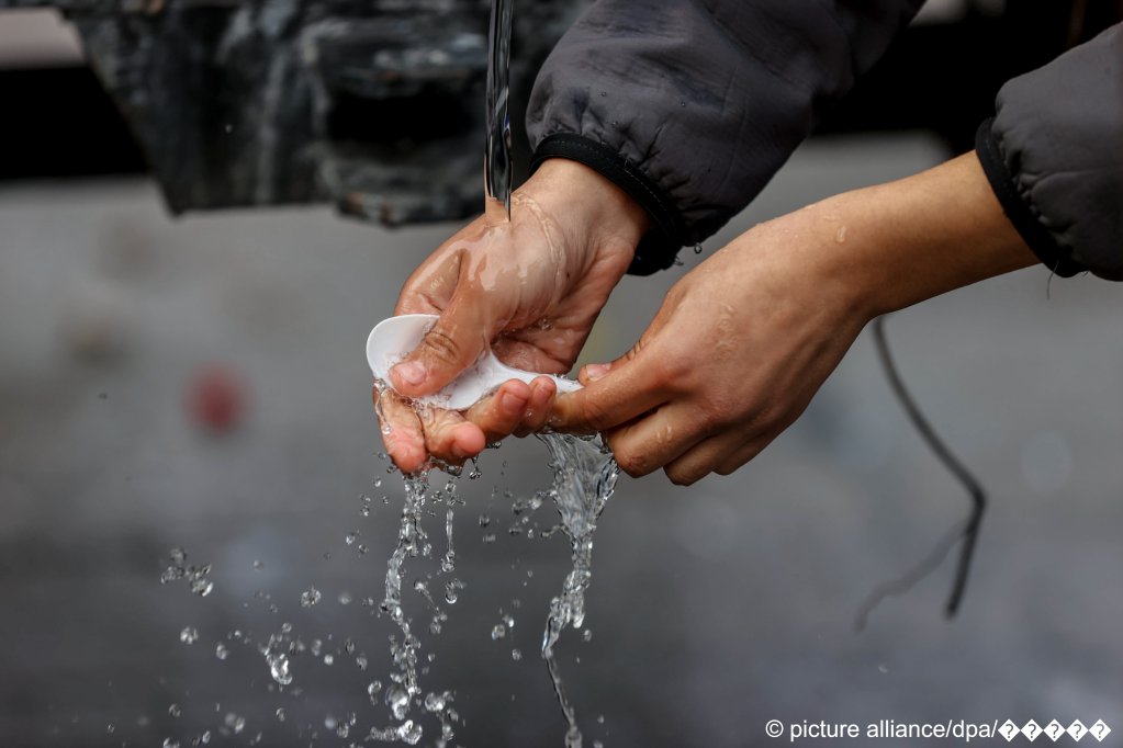 A migrant washes a plastic spoon outside the Bruzgi transport and logistics center on November 22, 2021 | Photo: Andrei Pokumeiko/BelTA/TASS/picture-alliance