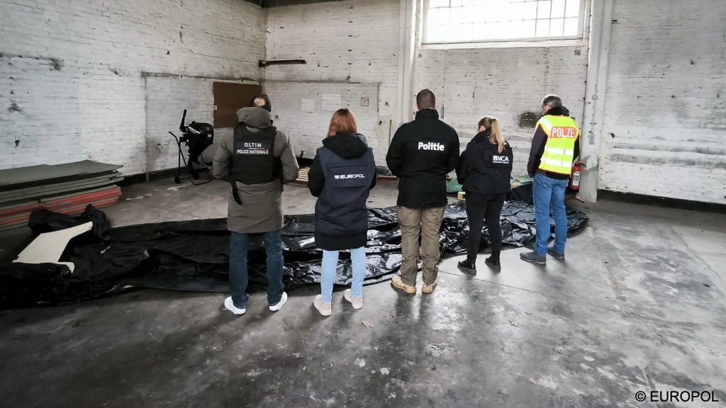 Officers from various national police forces and Europol stand near a deflated rubber dinghy in a warehouse, one of the finds from the raids conducted across Europe on March 25 | Photo: Europol press office