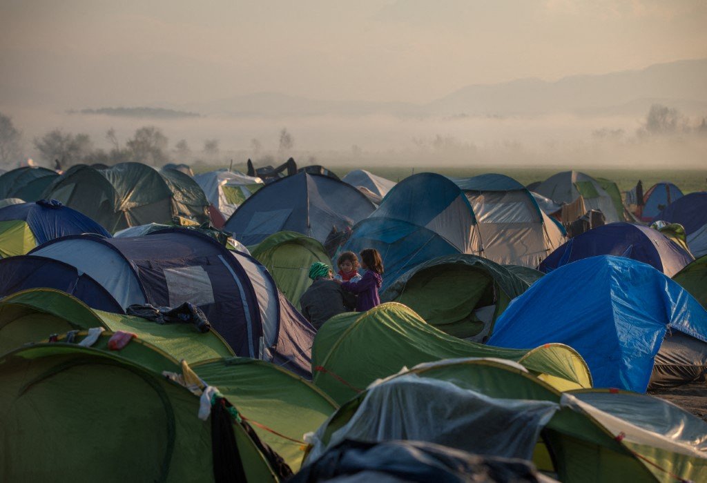 Smoke rises in the distance behind a woman standing among tents in a makeshift camp at the Greek-Macedonian border near the Greek village of Idomeni on March 3, 2016. Photo: AFP