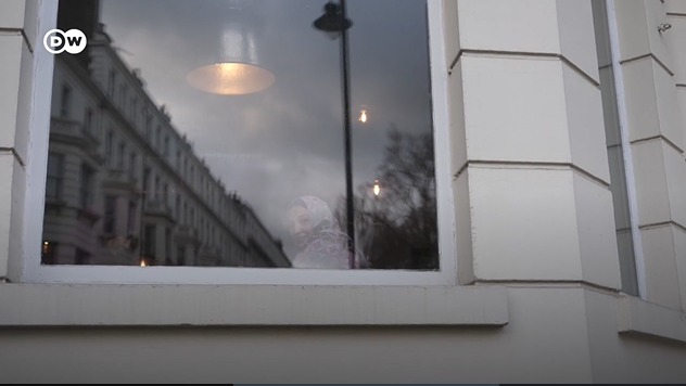 An Afghan woman sits in the window of the hotel which had accommodated Afghan refugees in London | Photo: Screenshot from DW report / DW / Kate Martyr