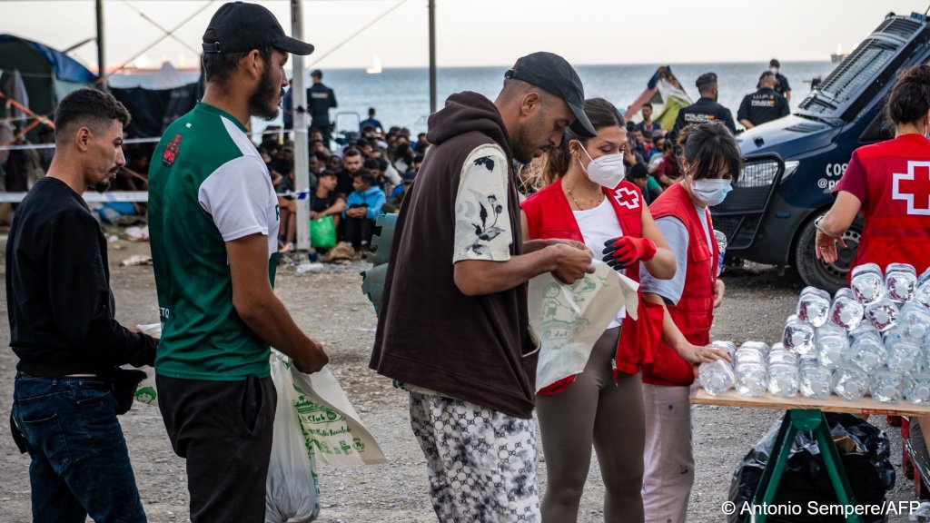 Red Cross workers hand out water at a food distribution point in a
temporary makeshift camp on an esplanade near the Trampolin beach to migrants waiting to be transferred to reception facilities in Ceuta on October 7, 2026 | Photo: Antonio Sempere/AFP