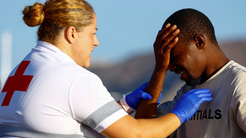 A Red Cross worker helps a migrant after disembarking from a boat towed by a Spanish coast guard vessel at the port of Arguineguin, on the island of Gran Canaria on October 11, 2026 | Photo: Borja Suarez/Reuters