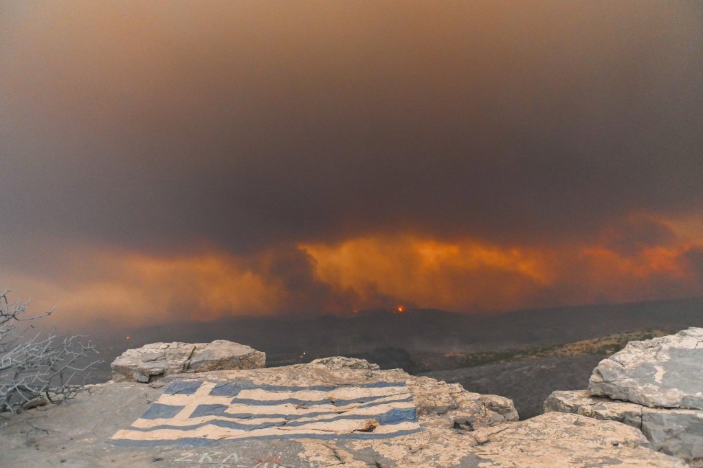 A painted Greek flag in the area of Makri with the background of the fire around Alexandroupolis, northern Greece. on August 22, 2023 | Photo: EPA/DIMITRIS ALEXOUDIS