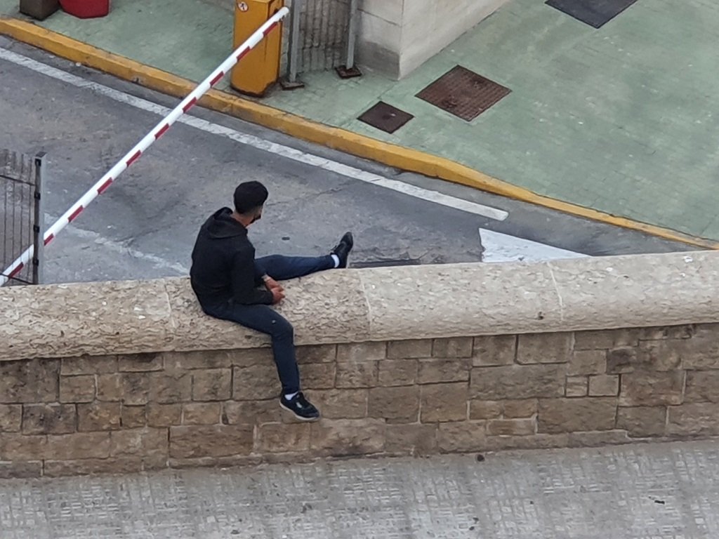 يراقب بعض المهاجرين محيط الميناء من على أسوار القلعة الأثرية المواجهة للميناء، 20 أيار/مايو 2021. شريف بيبي / مهاجر نيوز