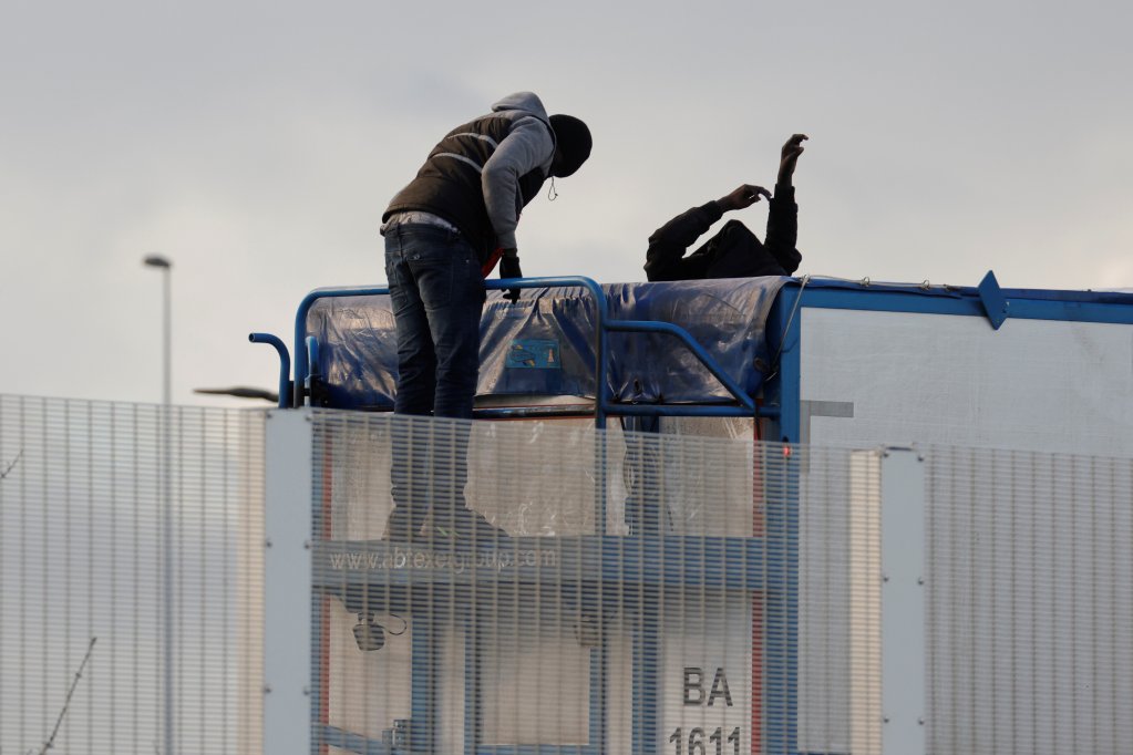 Deux exilés tentent de monter dans un camion, près du tunnel sous la Manche. Crédit : Reuters