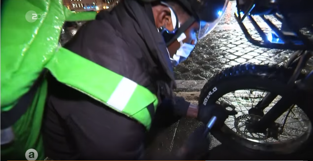 James Osawe regonfle le pneu de son scooter à la Piazza Venezia de Rome. Ce temps passé va lui coûter des points. | Source : Capture d’écran du reportage de la ZDF